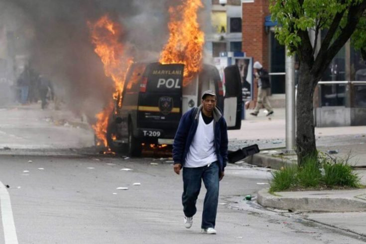 A man walks past a burning police vehicle, Monday, April 27, 2015, during unrest following the funeral of Freddie Gray in Baltimore. Gray died from spinal injuries about a week after he was arrested and transported in a Baltimore Police Department van. (AP Photo/Patrick Semansky)